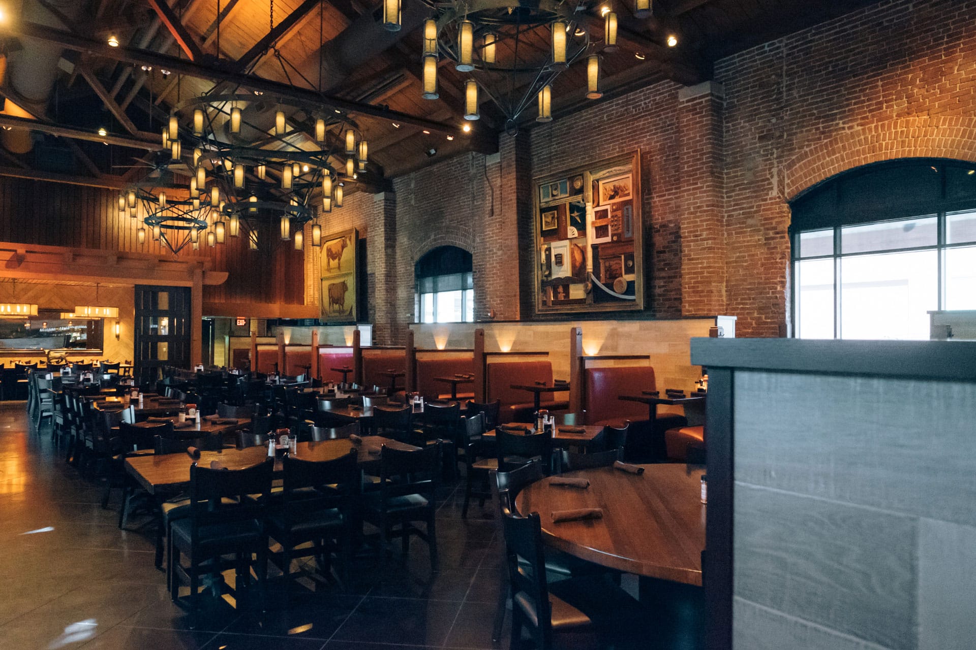 Spacious restaurant interior with exposed brick, tall vaulted ceilings, wrought-iron chandeliers, and dark wood tables.