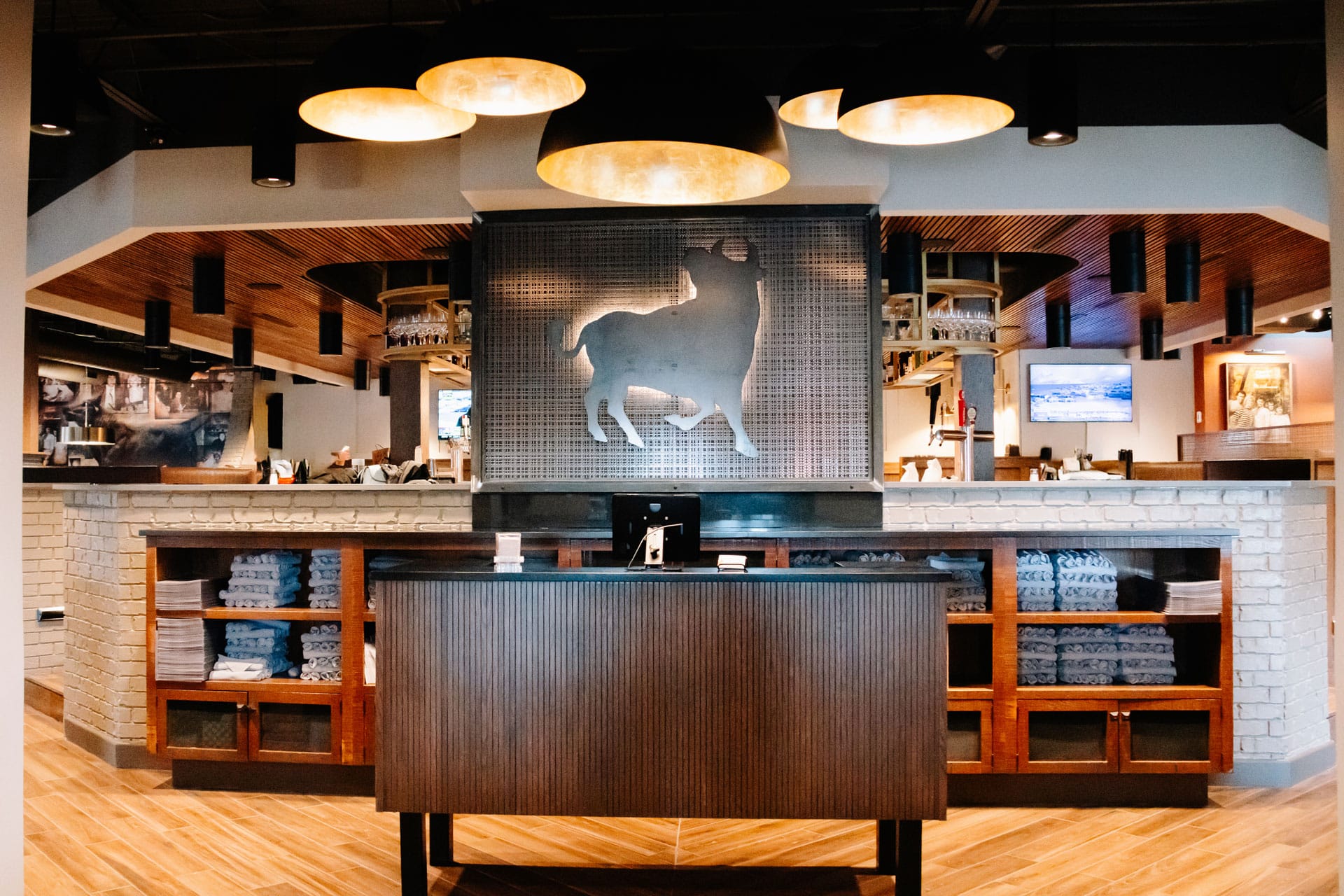 Symmetrical view of a wooden host stand under warm gold dome lights with a metal bull logo backdrop.